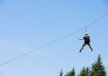 Rear view of young man riding on zip line against blue sky